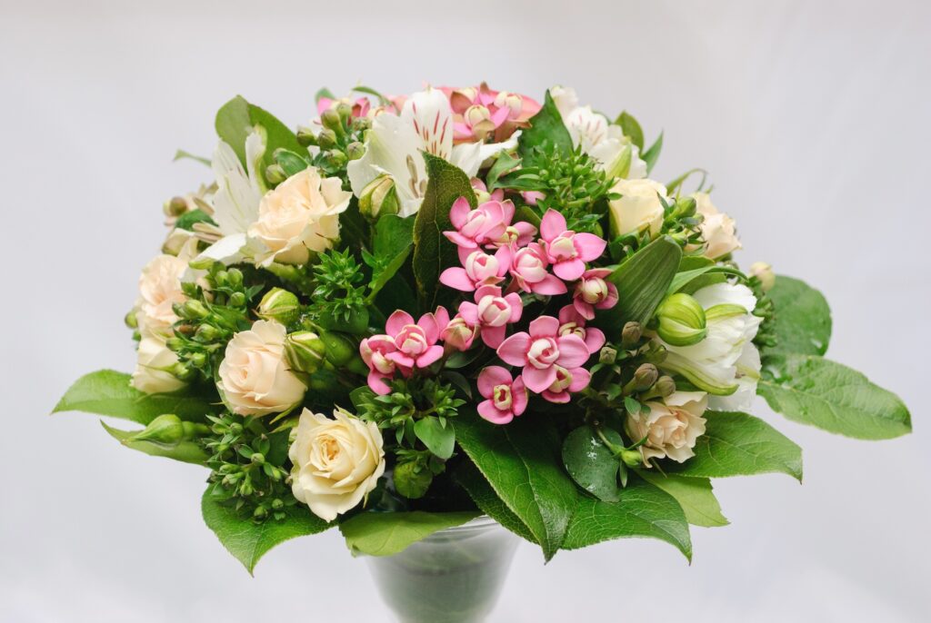 A bouquet of cream roses, white lilies and pink florals in the center is accentuated with lemon leaves, providing a rich green backdrop and contrast.